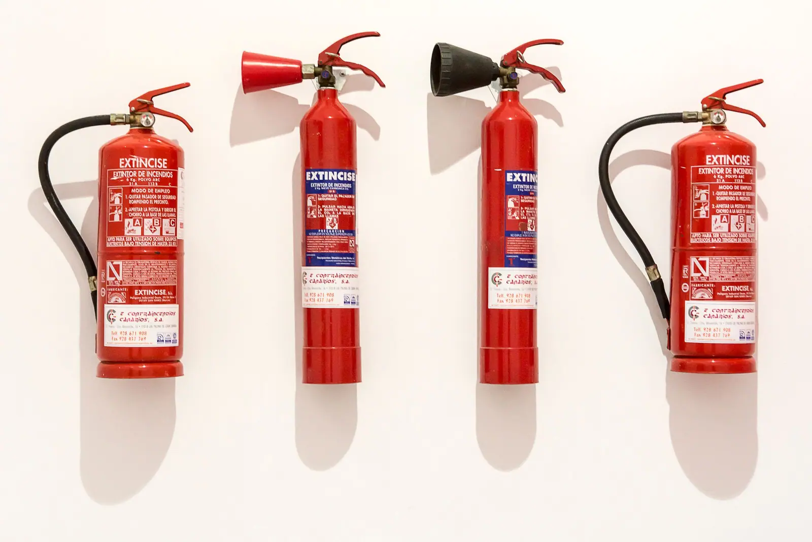 Four red portable fire extinguishers mounted on a white wall