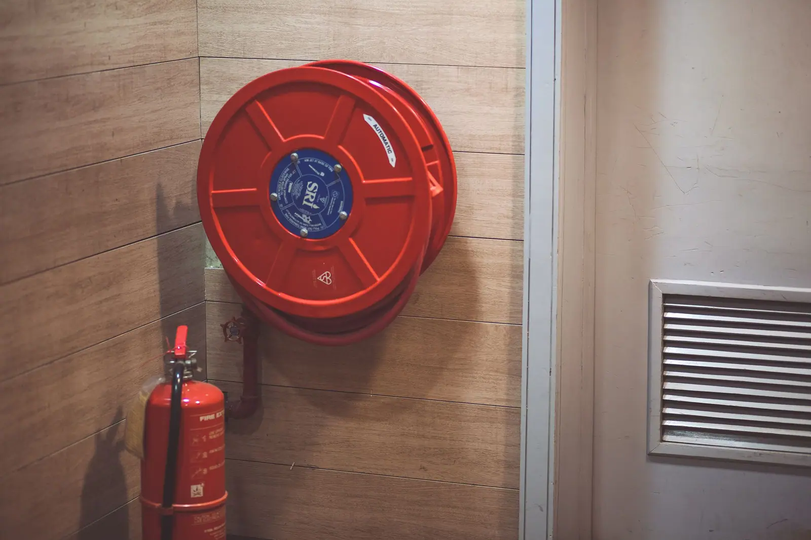 Red fire hose reel and a portable extinguisher mounted on a building wall